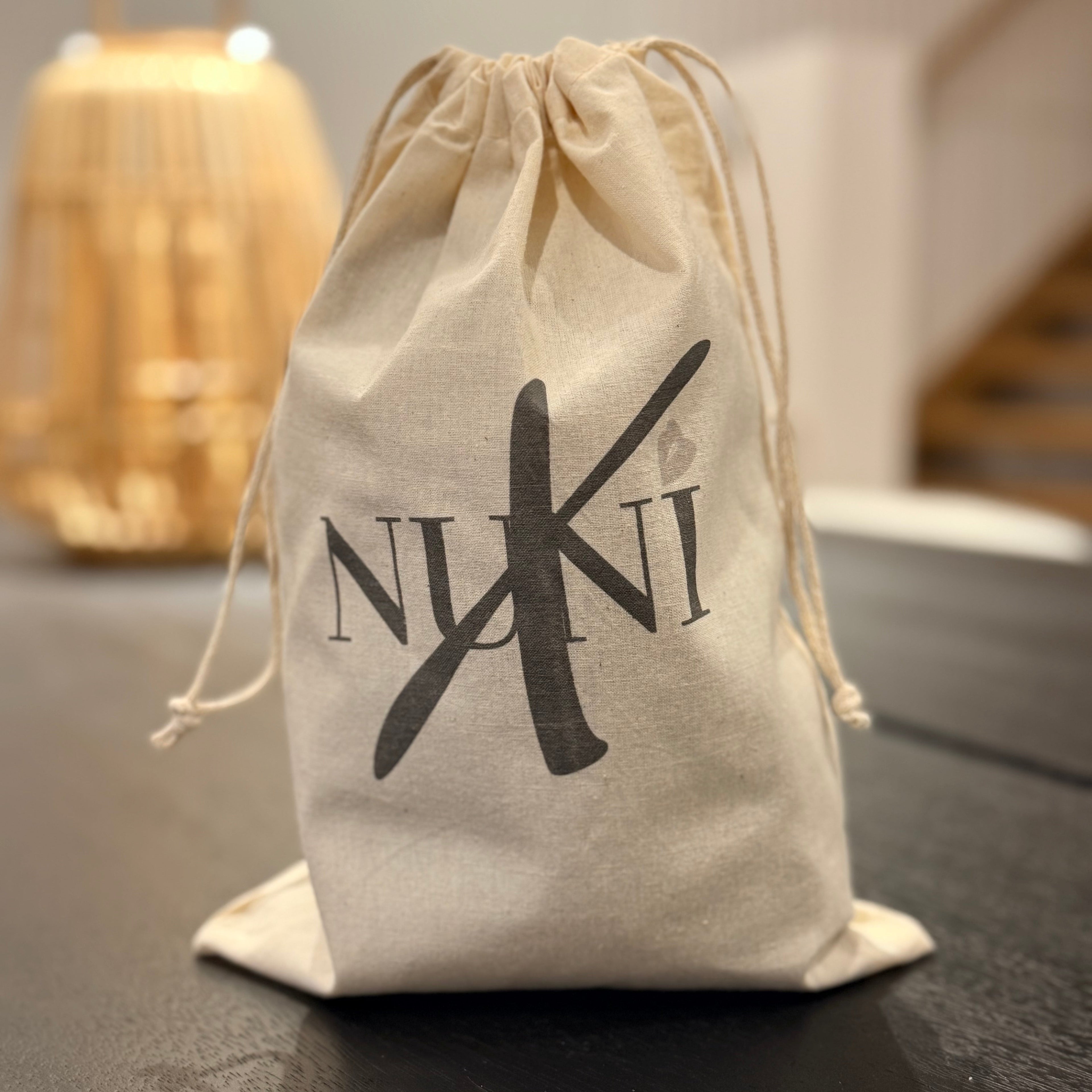Beige drawstring bag with 'Nuki' logo on a dark surface